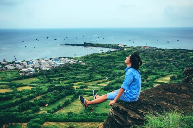 man sitting on a cliff looking at sky