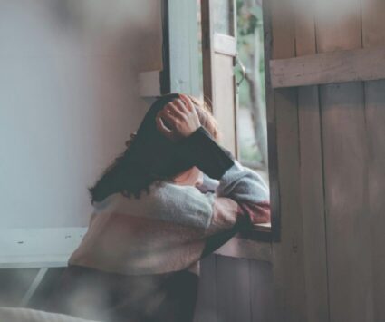 woman with hands on her head looking out of the open window